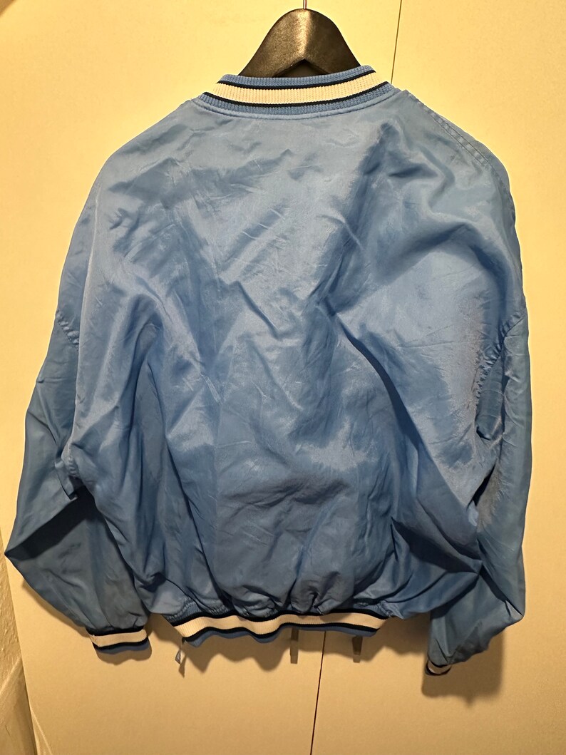 K&ouml;nnte beinhalten: Eine hellblaue Bomberjacke mit wei&szlig;en und dunkelblauen Rippb&uuml;ndchen an Kragen, &Auml;rmelb&uuml;ndchen und Saum.