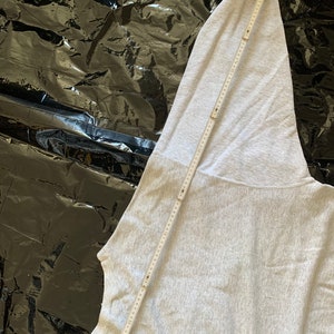 K&ouml;nnte beinhalten: Ein grauer Kapuzenpullover mit einem langen &Auml;rmel. Der &Auml;rmel liegt flach und wird mit einem Lineal gemessen.