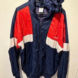May include: A blue, red and white windbreaker jacket with a zip fastening and a hood. The jacket features the Adidas logo on the right side of the chest.