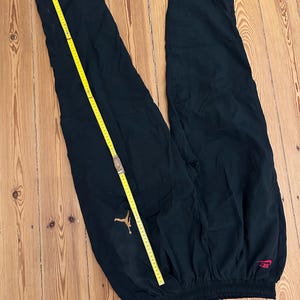 K&ouml;nnte beinhalten: Schwarze Sporthose mit goldenem Jordan-Logo und rotem Nike-Logo. Ein gelbes Ma&szlig;band liegt &uuml;ber der Hose. Die Hose besteht aus leichtem Material und hat einen elastischen Bund.