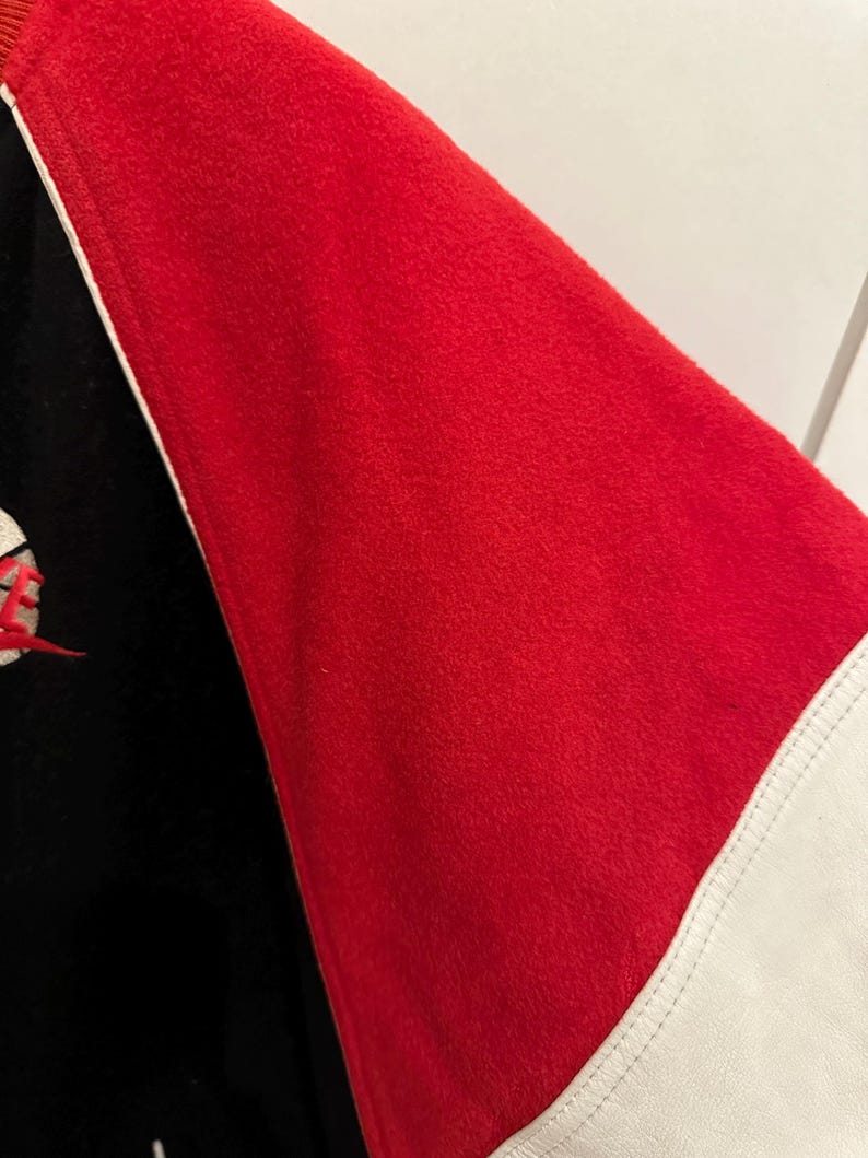 May include: Close-up of a red and black jacket sleeve. The sleeve is red with a white stripe and a black section. The jacket appears to be made of a soft, textured material.