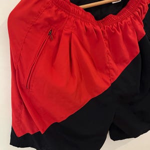 May include: Red and black athletic shorts with a Nike logo on the side and a zippered pocket. The shorts have an elastic waistband.