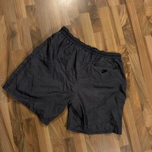 May include: Black nylon athletic shorts with a zippered pocket on the right side and a small black logo on the pocket.