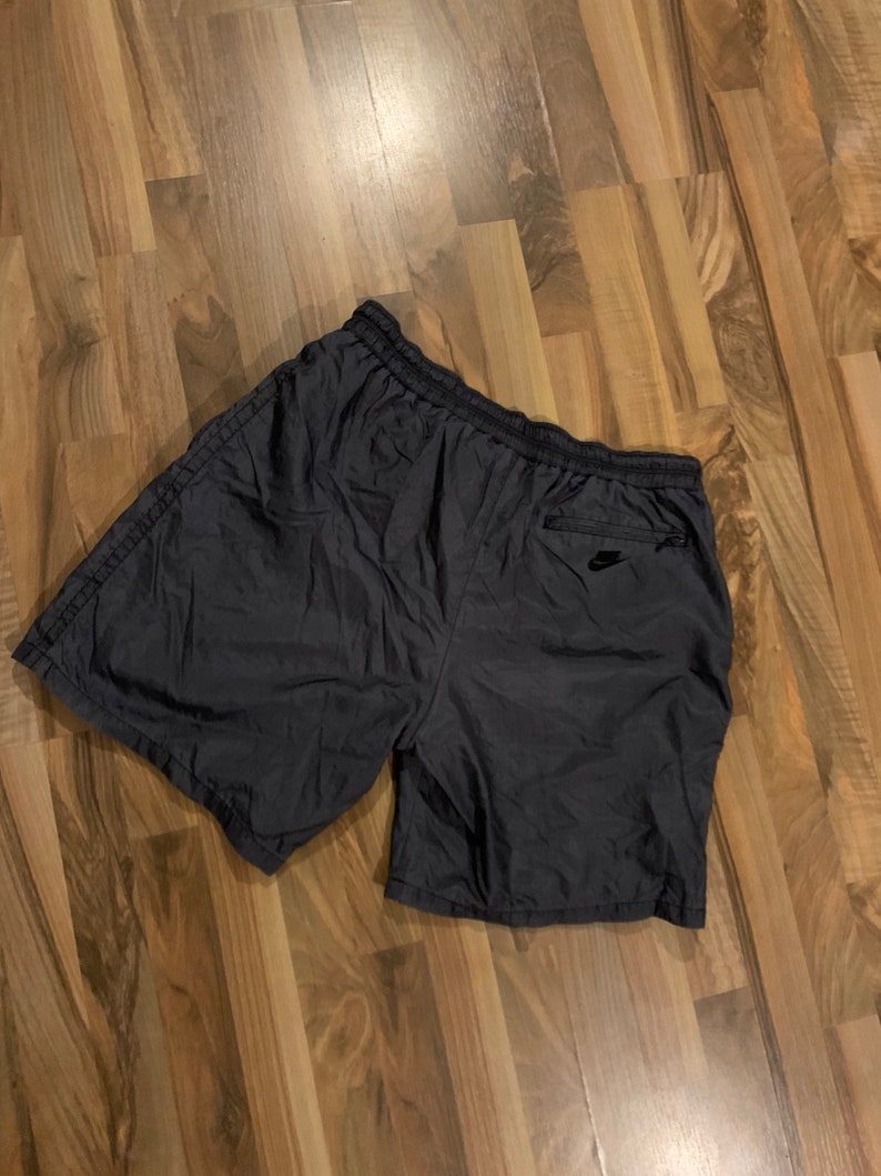 May include: Black nylon athletic shorts with a zippered pocket on the right side and a small black logo on the pocket.