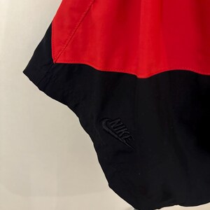 May include: Black and red Nike windbreaker with a black Nike logo on the bottom right side.