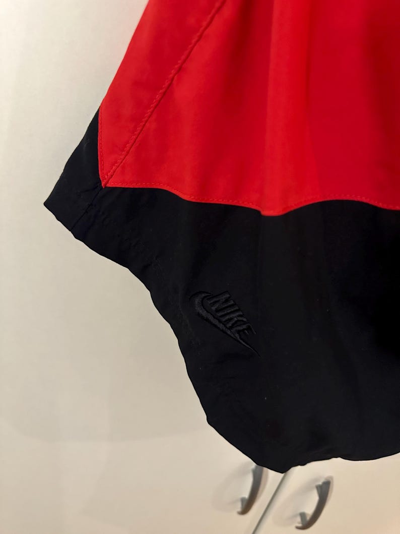 May include: Black and red Nike windbreaker with a black Nike logo on the bottom right side.