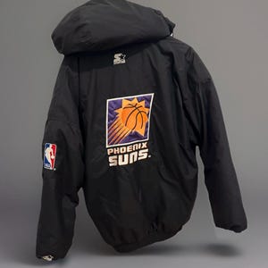 Può includere: Giacca nera con cappuccio con il logo dei Phoenix Suns sul retro. Il logo include un pallone da basket e le parole "Phoenix Suns". Una toppa con il logo NBA è sulla manica sinistra. La giacca ha un logo Starter sul cappuccio.