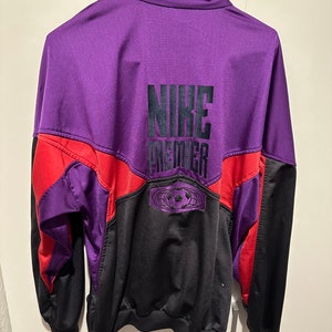 Könnte beinhalten: Eine violette, rote und schwarze Nike Premier Trainingsjacke mit einem schwarzen gestickten Logo auf der Rückseite.