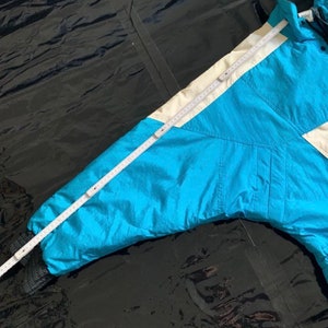 May include: A blue ski jacket with a white stripe down the sleeve. The jacket has a zipper closure and a hood.