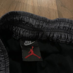 May include: A black Nike Jordan brand label with a white Nike swoosh and a red Jumpman logo.
