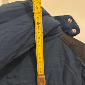 May include: A navy blue jacket with a yellow and white patch. A yellow measuring tape shows a length of approximately 30 inches. The jacket has a black collar and snap closures.