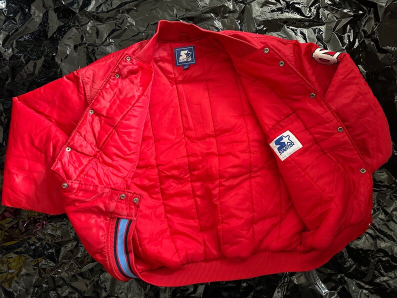 May include: Red Starter brand bomber jacket with blue and white trim. The jacket has a quilted lining and a snap closure.