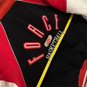 May include: A vintage black, red, and white Nike varsity jacket. The jacket features the word "FORCE" in red and white lettering, with "BASKETBALL" below. The jacket has white leather sleeves and a red collar and back.