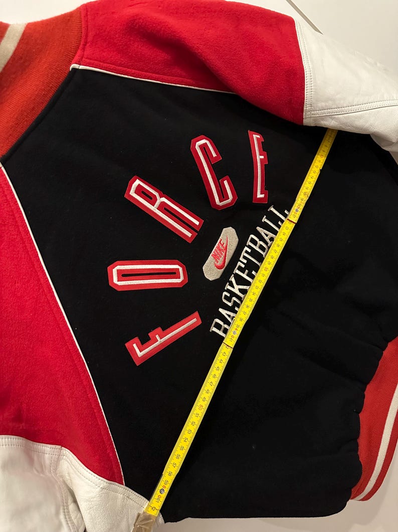 May include: A vintage black, red, and white Nike varsity jacket. The jacket features the word "FORCE" in red and white lettering, with "BASKETBALL" below. The jacket has white leather sleeves and a red collar and back.