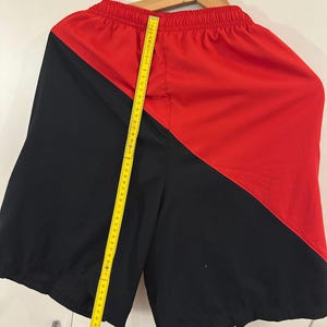 May include: Black and red athletic shorts with a diagonal color block design. The shorts have an elastic waistband and a drawstring.