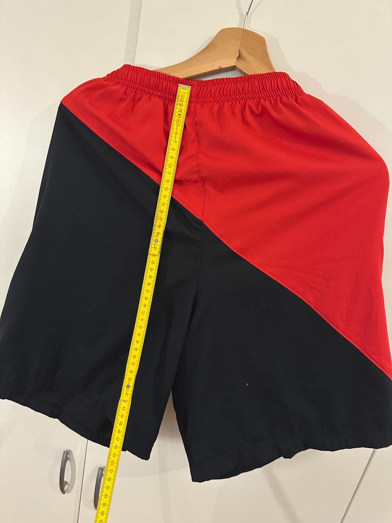 May include: Black and red athletic shorts with a diagonal color block design. The shorts have an elastic waistband and a drawstring.