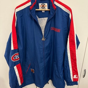 Könnte beinhalten: Eine blaue Windbreaker-Jacke der Marke Starter mit roten und weißen Streifen an den Ärmeln. Die Jacke hat das Logo der Montreal Canadiens auf dem linken Ärmel und den Teamnamen "Canadiens" auf der Vorderseite. Die Jacke hat einen Reißverschluss und eine Kapuze mit Kordelzug.