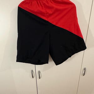 May include: Black and red athletic shorts with a diagonal color block design.