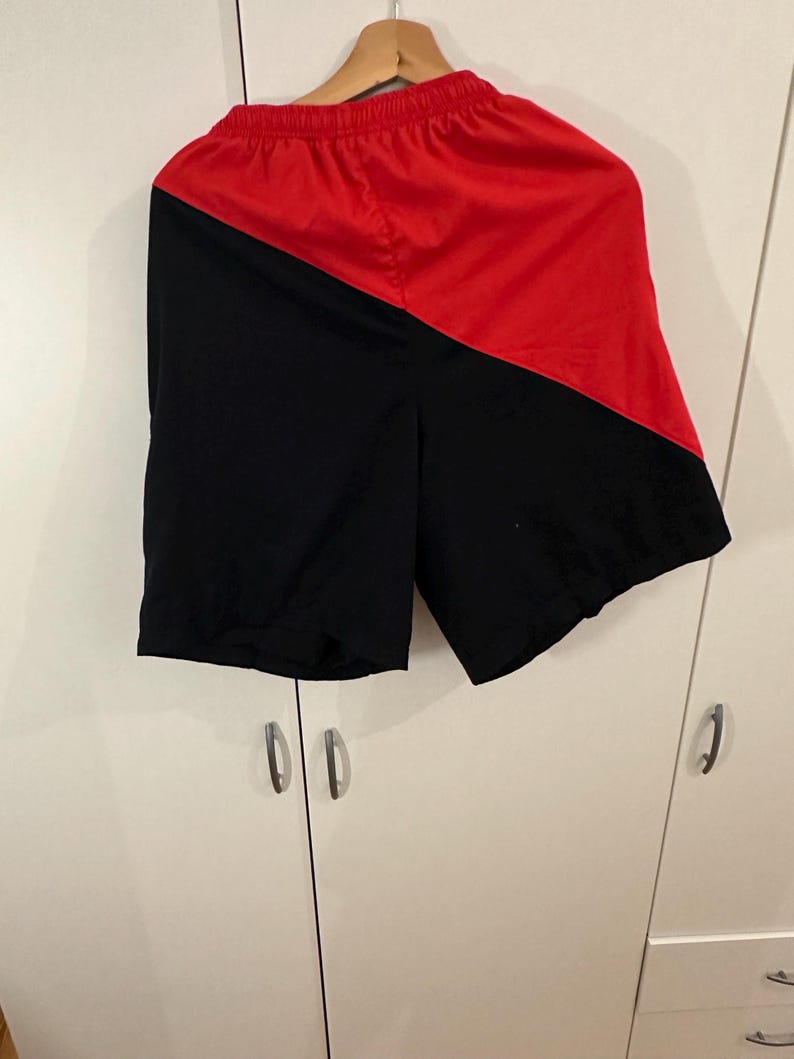 May include: Black and red athletic shorts with a diagonal color block design.