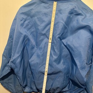 K&ouml;nnte beinhalten: Eine hellblaue Jacke mit wei&szlig;en und schwarzen Einfassungen an Kragen, &Auml;rmelb&uuml;ndchen und Saum. Die Jacke hat einen Rei&szlig;verschluss und einen Kordelzug in der Taille. Die Jacke wird mit einem Ma&szlig;band gemessen und zeigt eine L&auml;nge von 147 cm.