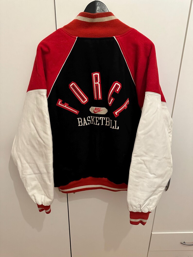May include: A vintage red, black, and white Nike basketball jacket. The jacket features red sleeves and collar, white leather sleeves, and a black back panel with "FORCE BASKETBALL" lettering. The Nike logo is visible.