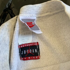 K&ouml;nnte beinhalten: Grauer Sweatshirt mit einem wei&szlig;en Etikett mit der Aufschrift "Authentic Jordan by Nike" und einem wei&szlig;en Etikett mit dem Nike-Logo und Pflegehinweisen. Das Etikett lautet "Made in U.S.A."