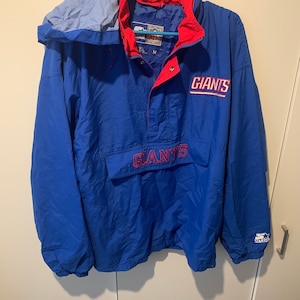 Könnte beinhalten: Eine blaue und rote New York Giants Anorakjacke. Die Jacke hat eine Kapuze, eine Vordertasche und das Wort "GIANTS" in roter Schrift auf der Brust und dem Rücken. Das Starter-Logo ist auf dem Ärmel sichtbar.
