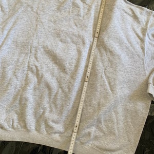 K&ouml;nnte beinhalten: Ein graues Sweatshirt mit einem Ma&szlig;band dar&uuml;bergelegt. Das Sweatshirt ist ein Basic-Modell mit Rundhalsausschnitt und langen &Auml;rmeln.