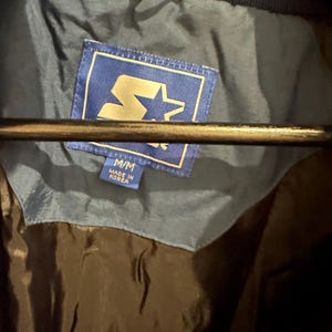 May include: A blue jacket with a Starter brand label. The label is blue with a gold star and the text "Starter". The jacket is size M/M and made in Korea.