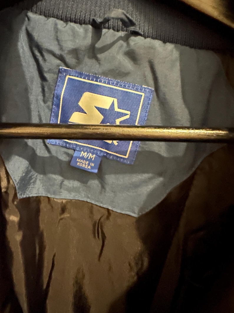 May include: A blue jacket with a Starter brand label. The label is blue with a gold star and the text "Starter". The jacket is size M/M and made in Korea.