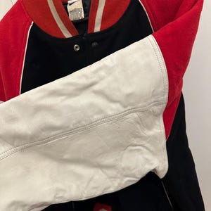May include: A vintage letterman jacket with a red, black, and white color scheme. The jacket features a red collar and cuffs, black body, and white leather sleeves. The jacket has a snap closure and a "FORCE" label.