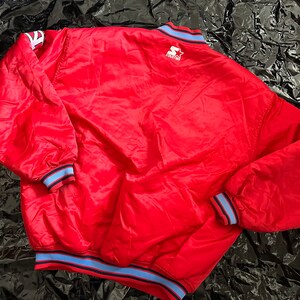 May include: A red satin bomber jacket with blue and white striped trim around the collar, cuffs, and hem. The jacket has a StarTech logo on the back.