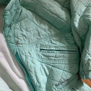May include: A quilted mint green jacket with a zipper closure and a zippered pocket on the left side. The jacket has a high collar and a white lining.