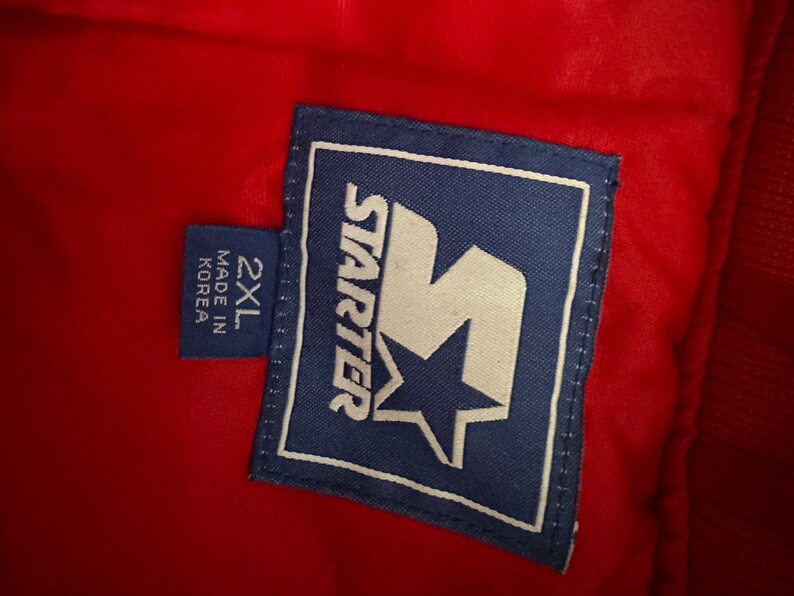 May include: A blue and white Starter brand label with a large white 'S' with a star inside. The label says 'Starter' and '2XL' and 'Made in Korea'.