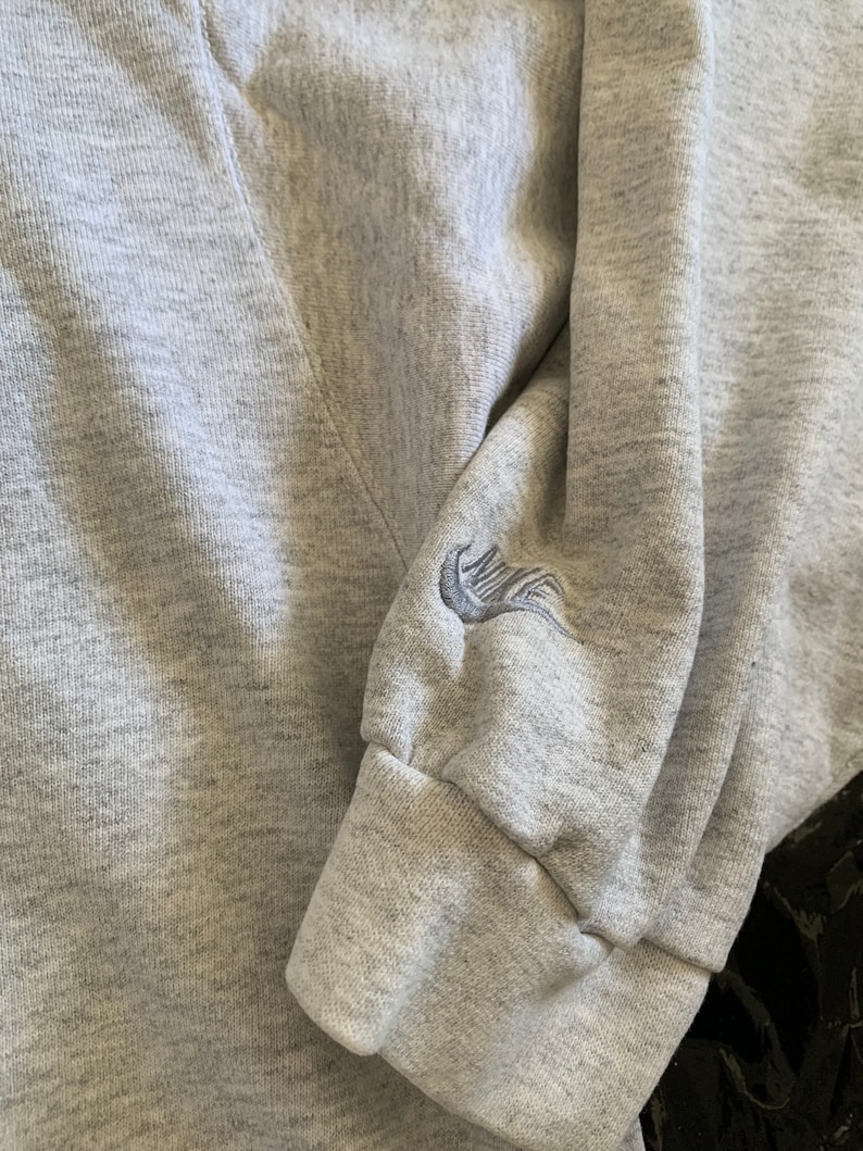 K&ouml;nnte beinhalten: Grauer Sweatshirt mit einem gestickten Nike-Logo auf dem &Auml;rmel.