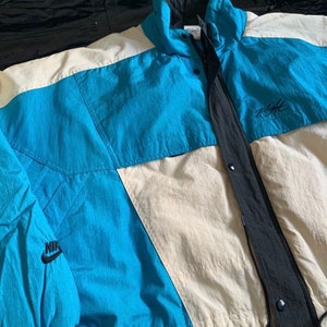 May include: A vintage Nike Flight jacket in blue, white, and black with a black Nike logo on the left sleeve. The jacket has a zipper closure and a drawstring hood.