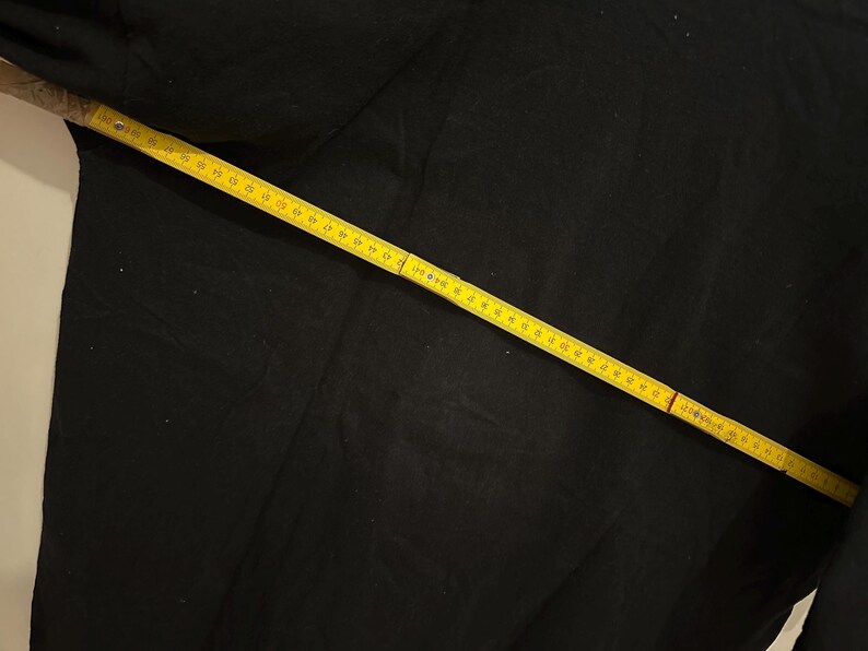 May include: A black fabric is measured with a yellow measuring tape. The tape is marked in centimetres and is laid diagonally across the fabric. The fabric appears to be a solid colour.