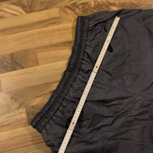 May include: Dark gray sweatpants with a drawstring waistband and a zippered pocket on the right side. A measuring tape is laid across the waistband.