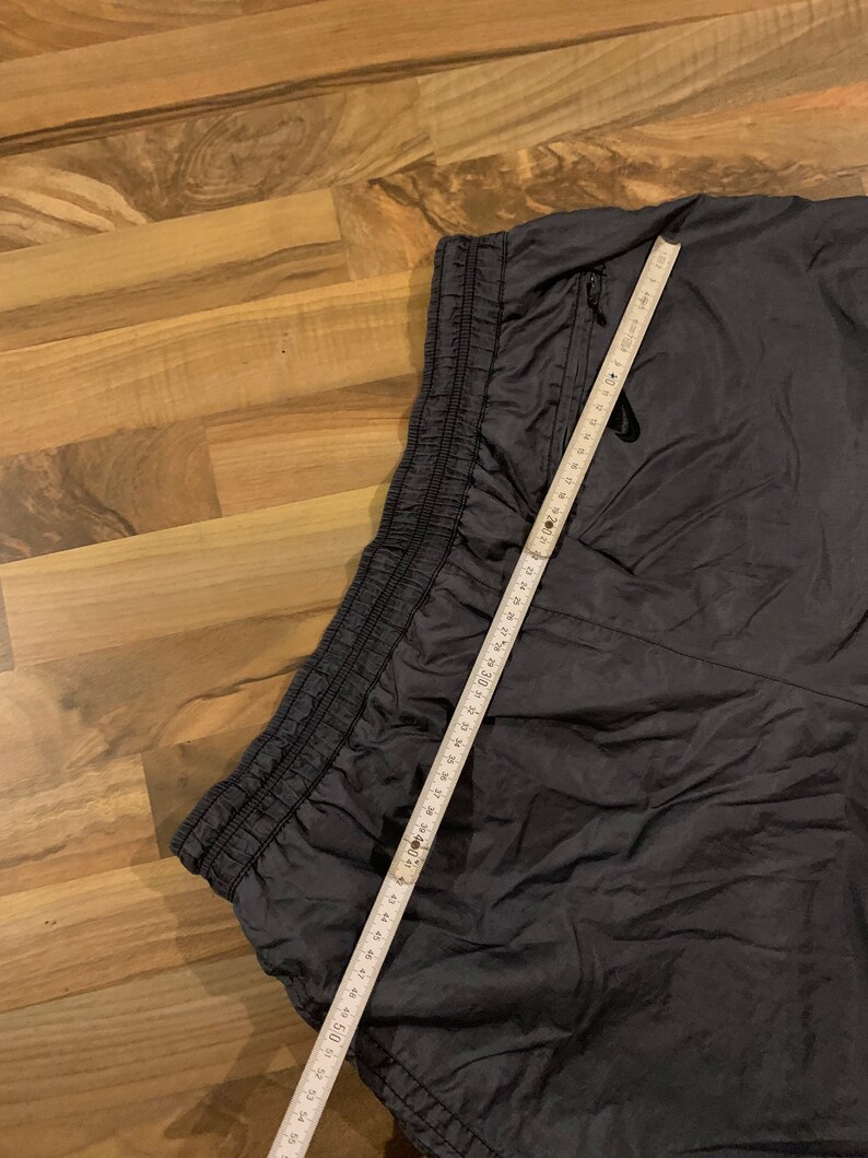 May include: Dark gray sweatpants with a drawstring waistband and a zippered pocket on the right side. A measuring tape is laid across the waistband.