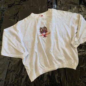 K&ouml;nnte beinhalten: Ein grauer Langarm-Sweatshirt mit einem Aufdruck eines Basketballspielers, der einen Dunk macht, mit dem Wort "AIR" &uuml;ber dem Spieler. Der Aufdruck ist in Schwarz, Orange und Pink.