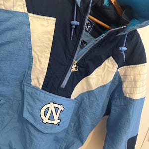 May include: A vintage Starter jacket in light blue, navy, and white. The jacket features a hood, a front pocket with a logo, and a zipper closure. The Starter logo is visible on the zipper pull.