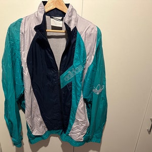 May include: A blue, white, and teal color-blocked windbreaker jacket with the word "adidas" in white lettering on the front.