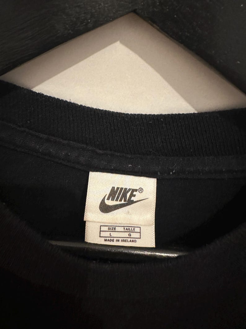 May include: Close-up of a black t-shirt collar with a Nike label. The label is white with black text, including the Nike logo, size information (L, G), and "MADE IN IRELAND".