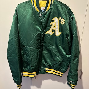 Könnte beinhalten: Eine grüne Satin-Baseballjacke mit gelben und weißen Streifen an Kragen, Ärmelbündchen und Bund. Die Jacke hat ein großes weißes "A's" auf der Vorderseite gestickt.