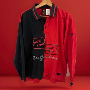 Peut inclure: Un polo à manches longues noir et rouge avec le numéro "23" et "Air Jordan" imprimé sur le devant. Le polo a un col rouge et des rayures rouges sur les manches.