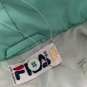 May include: A white Fila brand label with a blue button and the text "Made in Italy" on a light green jacket.
