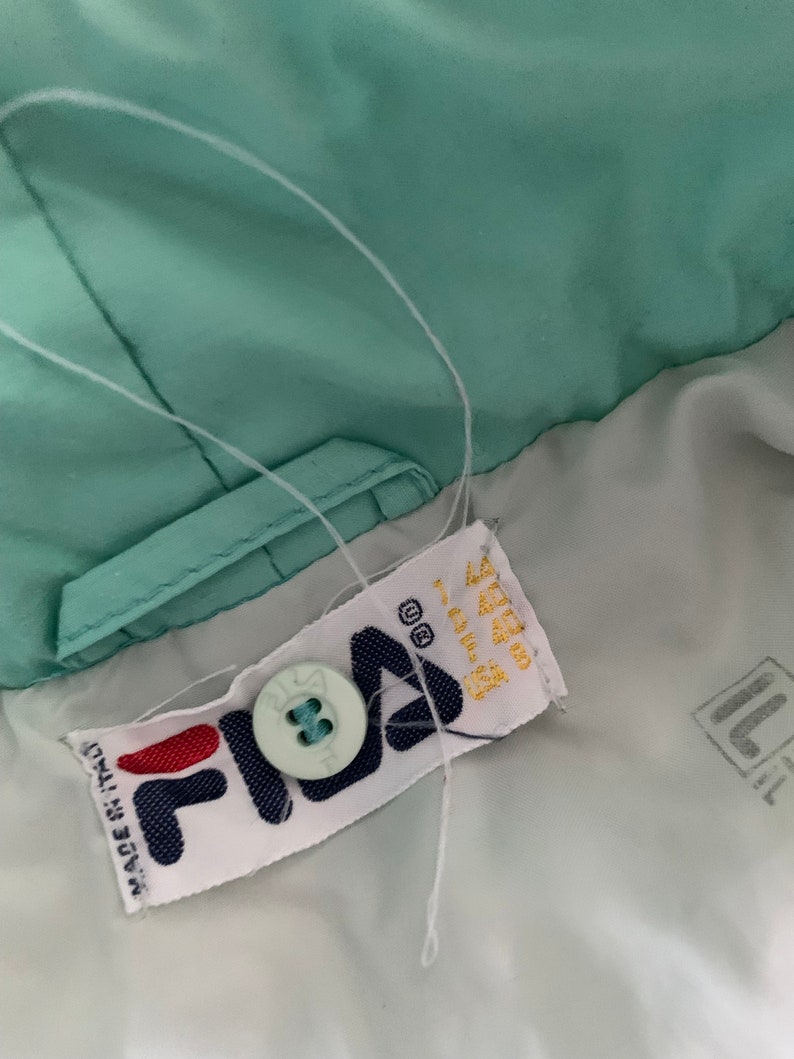 May include: A white Fila brand label with a blue button and the text "Made in Italy" on a light green jacket.