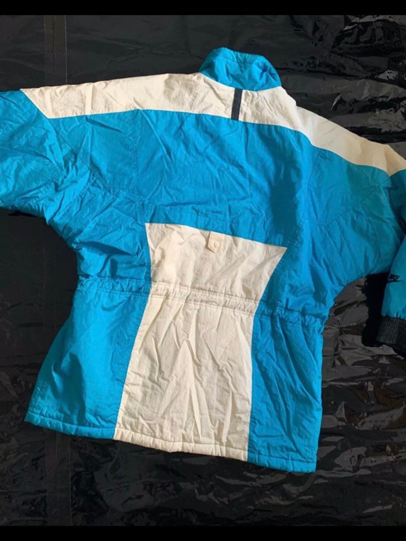 May include: A blue and white ski jacket with a zipper closure and a drawstring waist.