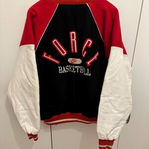 May include: Red, black, and white varsity jacket with "FORCE BASKETBALL" text on the back. The jacket has white sleeves, a red body, and a black back panel. The Nike logo is visible.