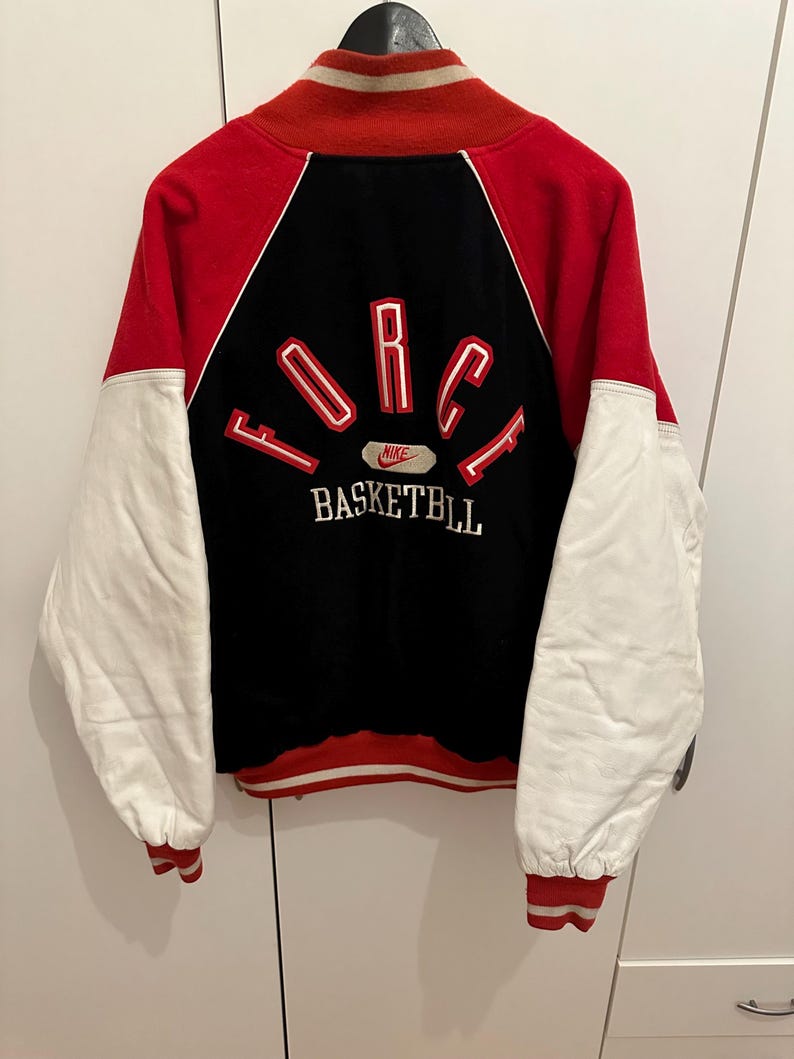 May include: Red, black, and white varsity jacket with "FORCE BASKETBALL" text on the back. The jacket has white sleeves, a red body, and a black back panel. The Nike logo is visible.